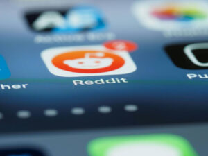 Close-up of the Reddit app icon on a cell phone with two notifications showing. Other app icons are in the background, out of focus.