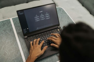 image showing a person typing a prompt into ChatGPT on a laptop. The image is taken from above the person, and we can only see the back of their head and their hands.