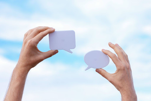 A person holding up two speech bubbles in each hand to depict “communication”